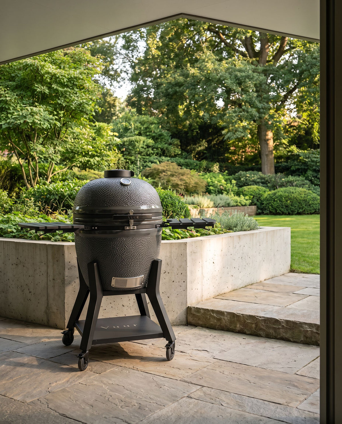 Grote kamado bij een lage tuinmuur die de schaal laat zien, geen personen.